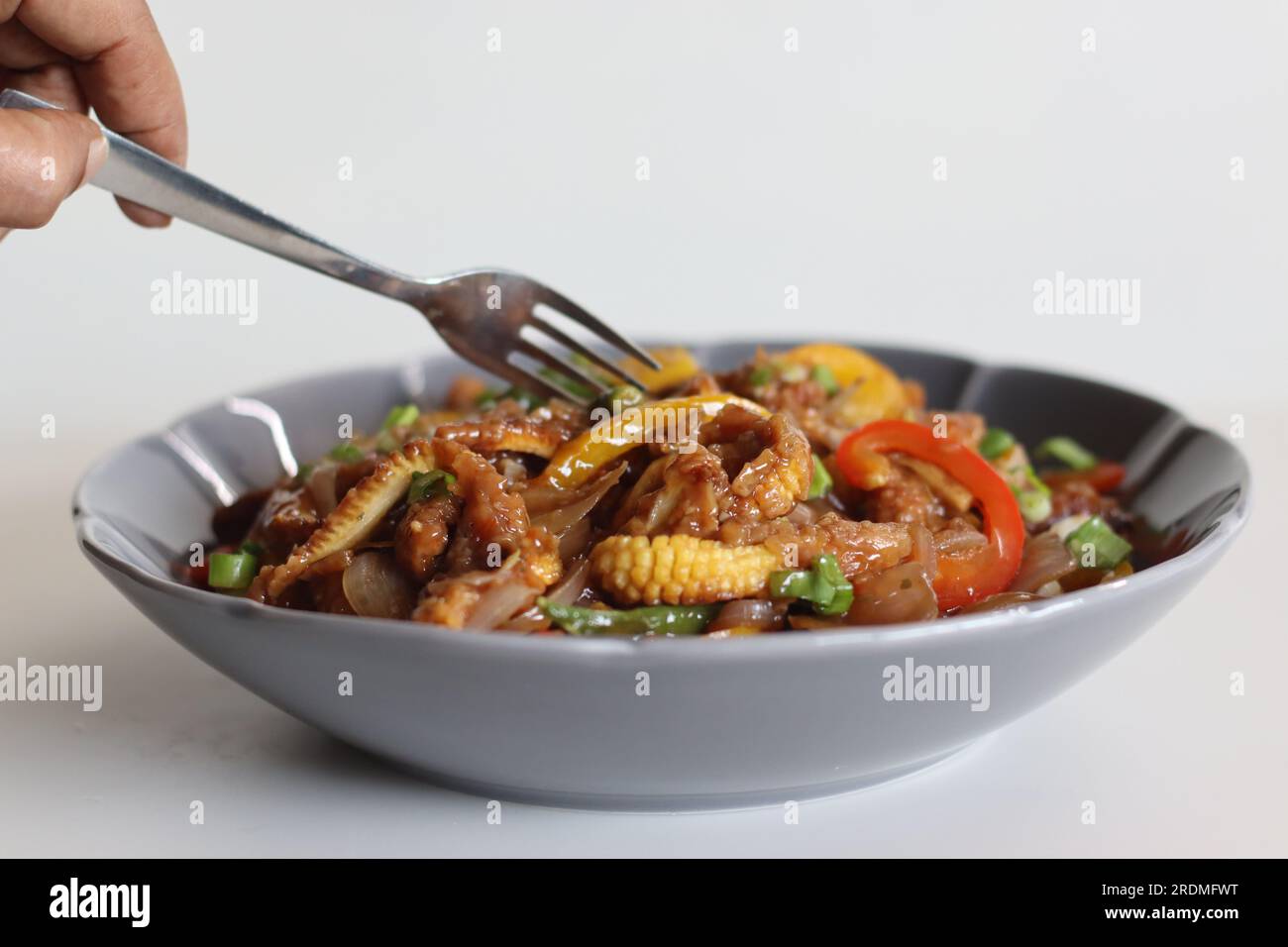 Baby corn freddo. Un piatto indo cinese con croccante mais fritto in una salsa piccante con cipolle saltate e peperoni. Ripresa su sfondo bianco Foto Stock