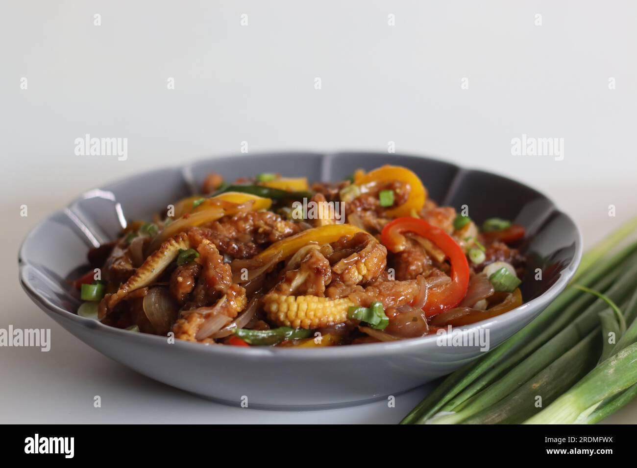 Baby corn freddo. Un piatto indo cinese con croccante mais fritto in una salsa piccante con cipolle saltate e peperoni. Ripresa su sfondo bianco Foto Stock