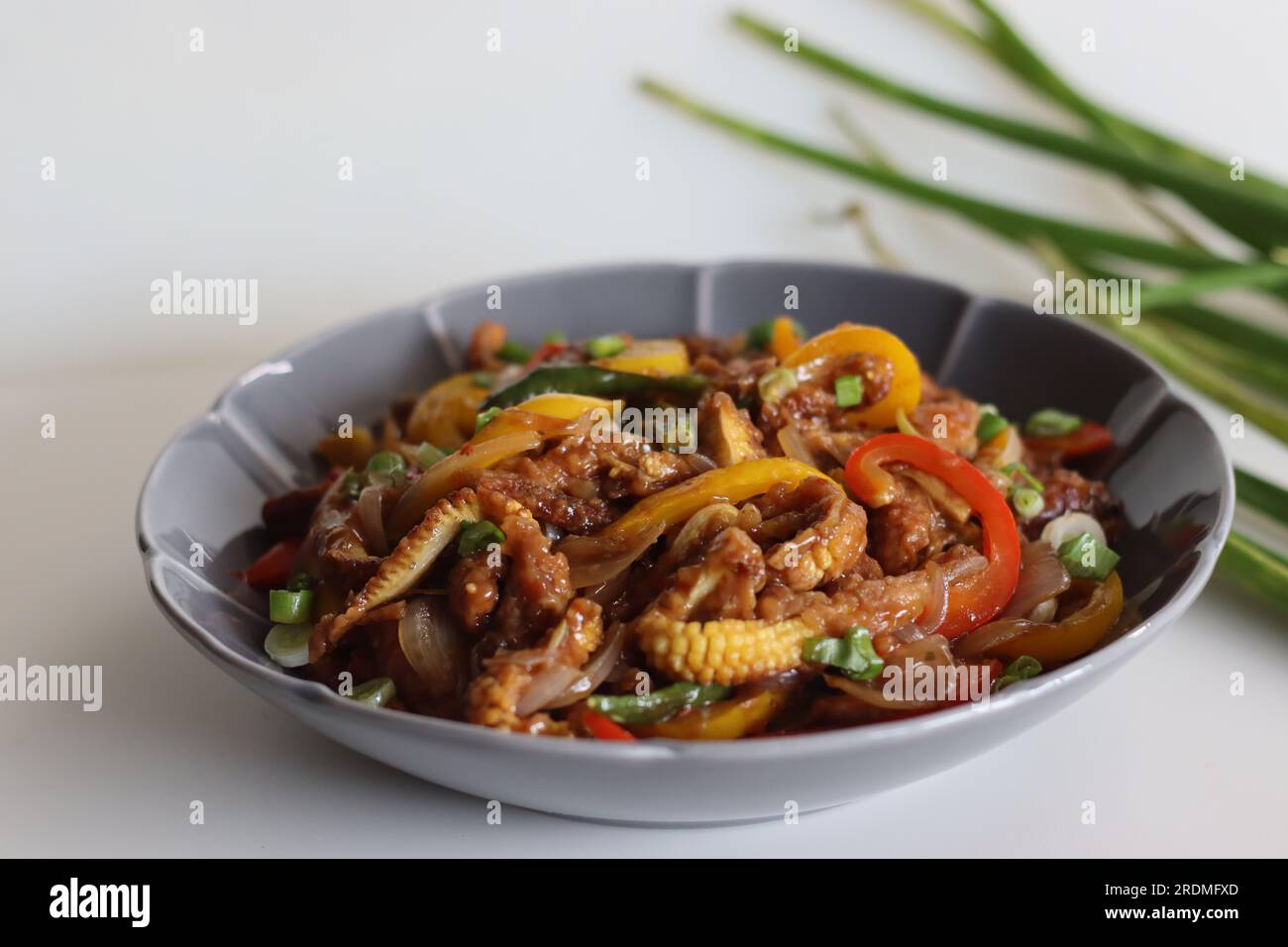 Baby corn freddo. Un piatto indo cinese con croccante mais fritto in una salsa piccante con cipolle saltate e peperoni. Ripresa su sfondo bianco Foto Stock