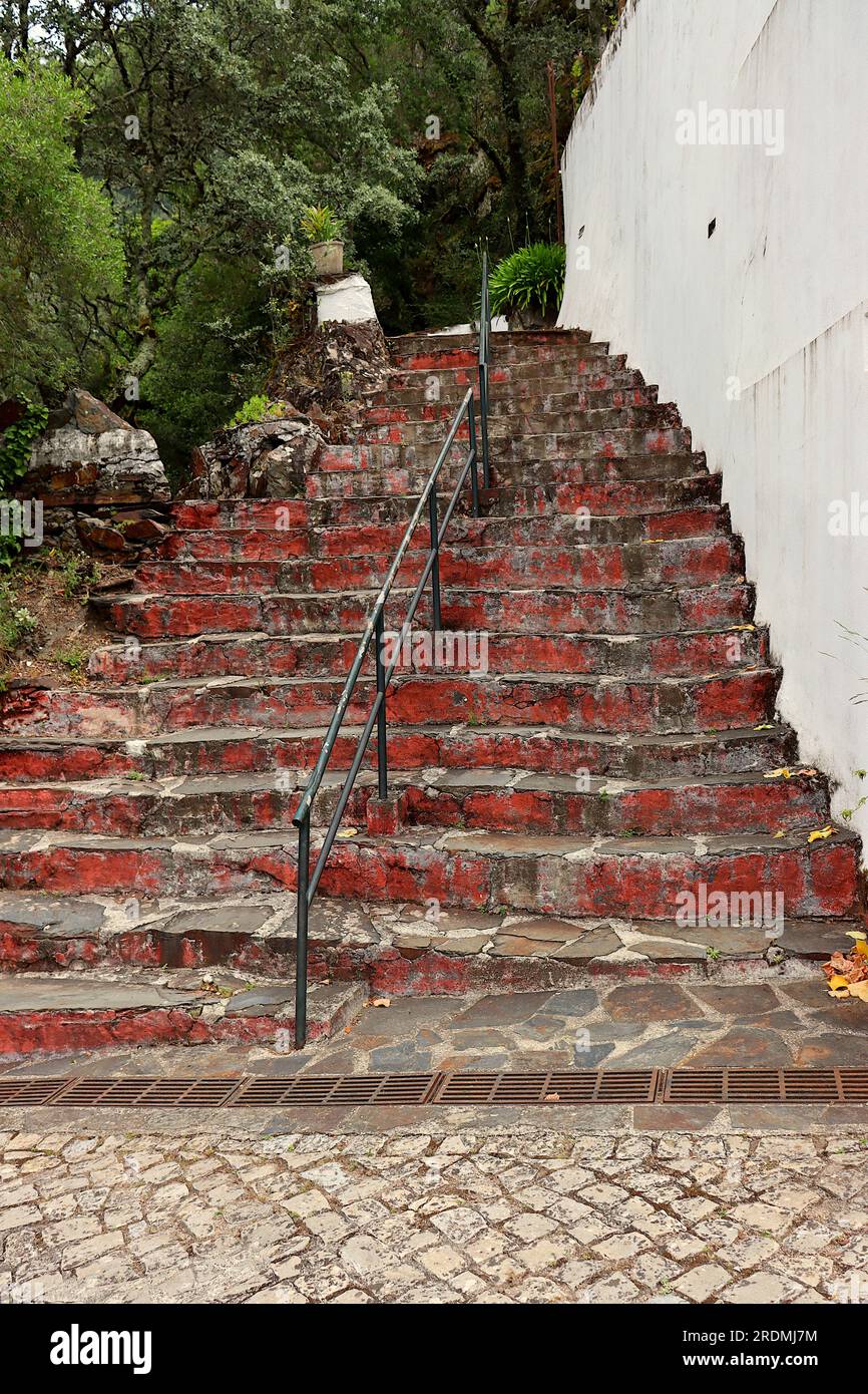 Scala con gradini in pietra, cemento dipinto di rosso e corrimano centrale in ferro. Accesso al Santuario di Nossa Senhora da Piedade, Lousã, Portogallo. Foto Stock