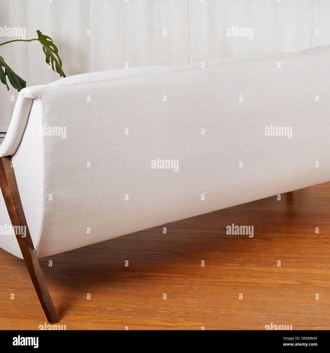 Divano vintage bianco. Elegante divano moderno della metà del secolo con gambe in legno scultoreo. Scena interna con tende bianche e pavimento in legno. Foto Stock