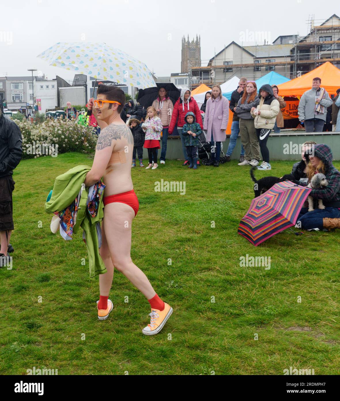 Cornwall Pride Newquay riceve piogge torrenziali e le attese migliaia di festaioli sono ridotte a circa un centinaio di duri. L'evento LGBTQ+ è stato un enorme successo negli anni precedenti. Spettatori con boccioli e un interprete con pantaloni rossi. Il cantante Benji Matthew, in cima bianca, ha un gruppo che balla sotto i loro ombrelli presso la sede di Killacourt nel centro della città. A Newquay, Cornovaglia, Regno Unito. 22 luglio 2023. Robert Taylor/Alamy Live News Foto Stock