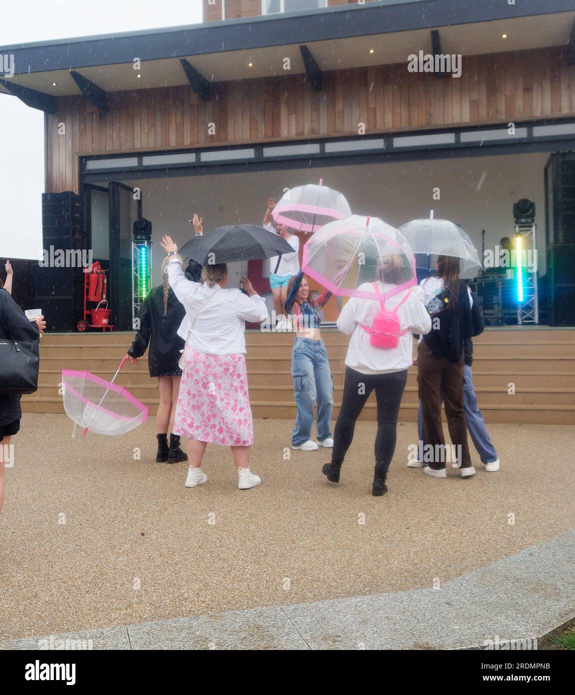 Cornwall Pride Newquay riceve piogge torrenziali e le attese migliaia di festaioli sono ridotte a circa un centinaio di duri. L'evento LGBTQ+ è stato un enorme successo negli anni precedenti. Spettatori con boccioli e un interprete con pantaloni rossi. Il cantante Benji Matthew, in cima bianca, ha un gruppo che balla sotto i loro ombrelli presso la sede di Killacourt nel centro della città. A Newquay, Cornovaglia, Regno Unito. 22 luglio 2023. Robert Taylor/Alamy Live News Foto Stock