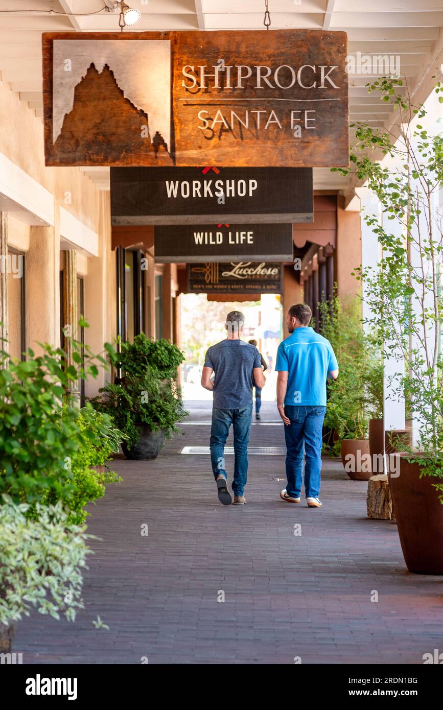 Due uomini in abito informale camminano lungo un marciapiede coperto che ha diversi cartelli appesi in Santa Fe Plaza, Santa Fe, New Mexico, USA. Foto Stock