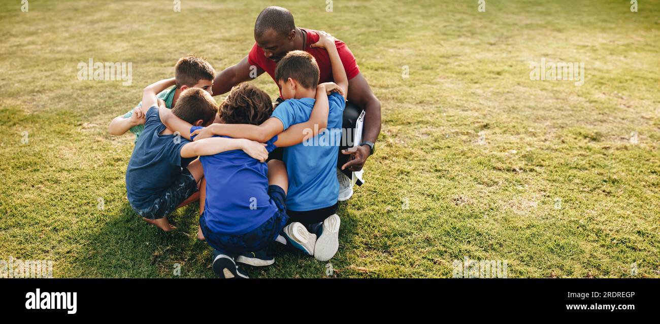 i bambini delle scuole si sono accarezzati con il loro allenatore in un campo sportivo. Istruttore che tiene un colloquio motivazionale con un gruppo di ragazzi delle scuole elementari. Sport e Foto Stock