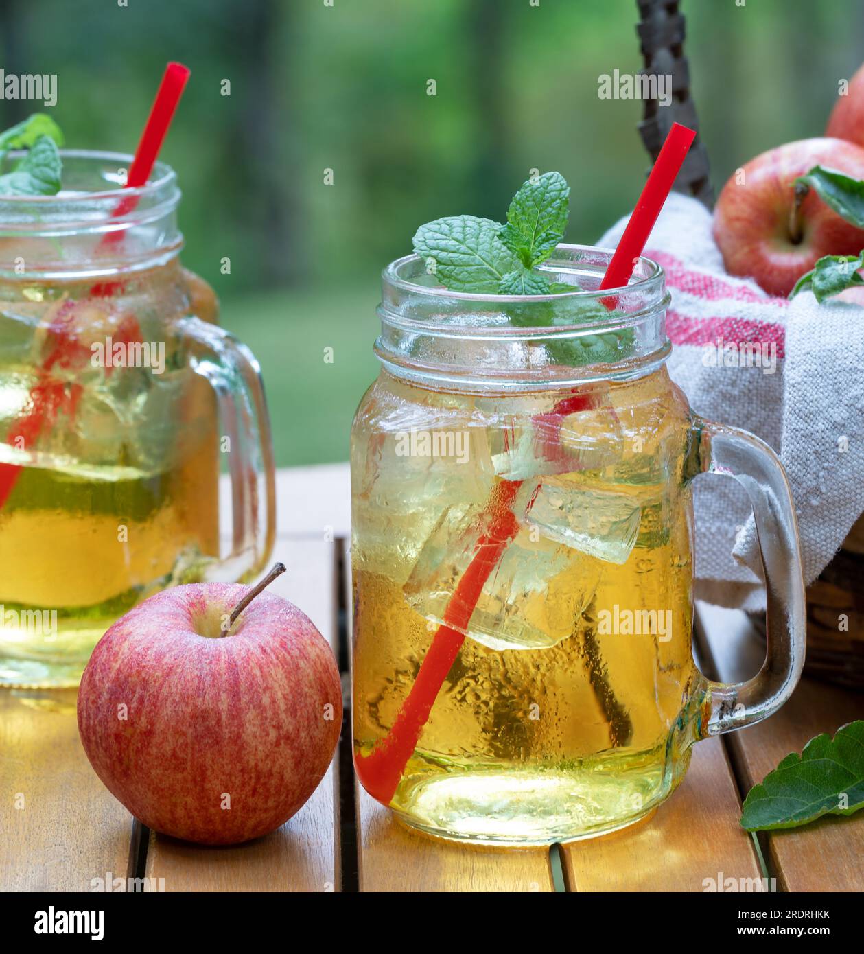 Succo di mela freddo in bicchieri con mele fresche all'aperto su un tabe del patio con sfondo naturale Foto Stock