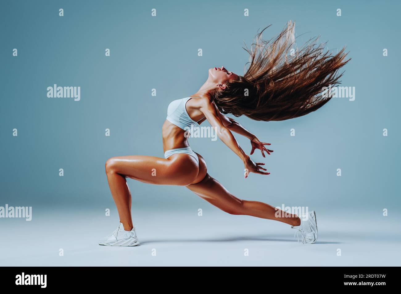 Giovane donna del fitness che balla e scuote i capelli su sfondo bianco Foto Stock