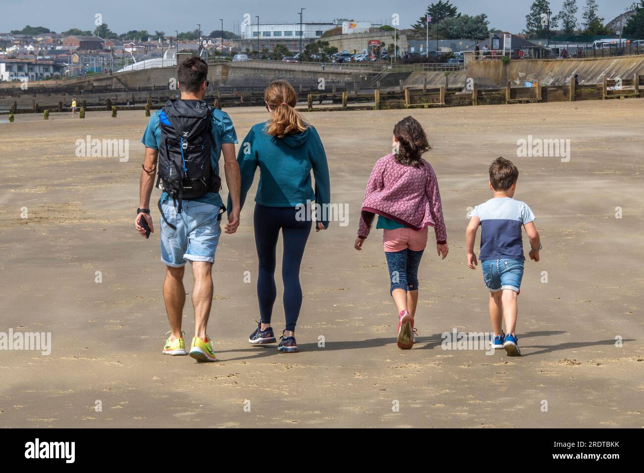una giovane famiglia che cammina insieme al mare in una giornata ventilata a sandown, sull'isola di wight, regno unito Foto Stock