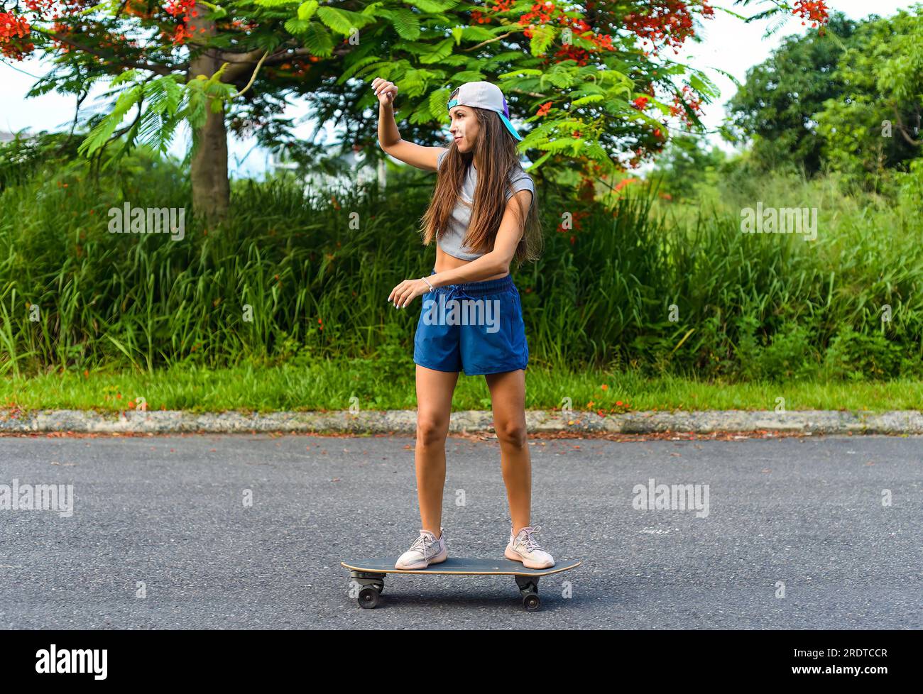 Giovane bella donna in berretto che cavalca uno skateboard e ride Foto Stock