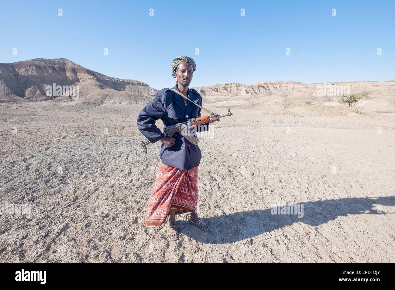 Un uomo etiope armato di mitragliatrice in piedi nel deserto. Guardia i turisti. Ritratto di un uomo in abiti tradizionali. Etiopia Foto Stock