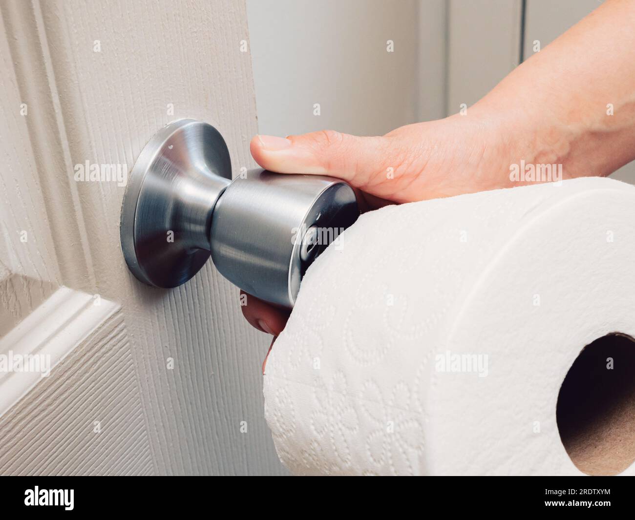 primo piano del pomello della porta del bagno con la carta igienica in mano. Foto Stock