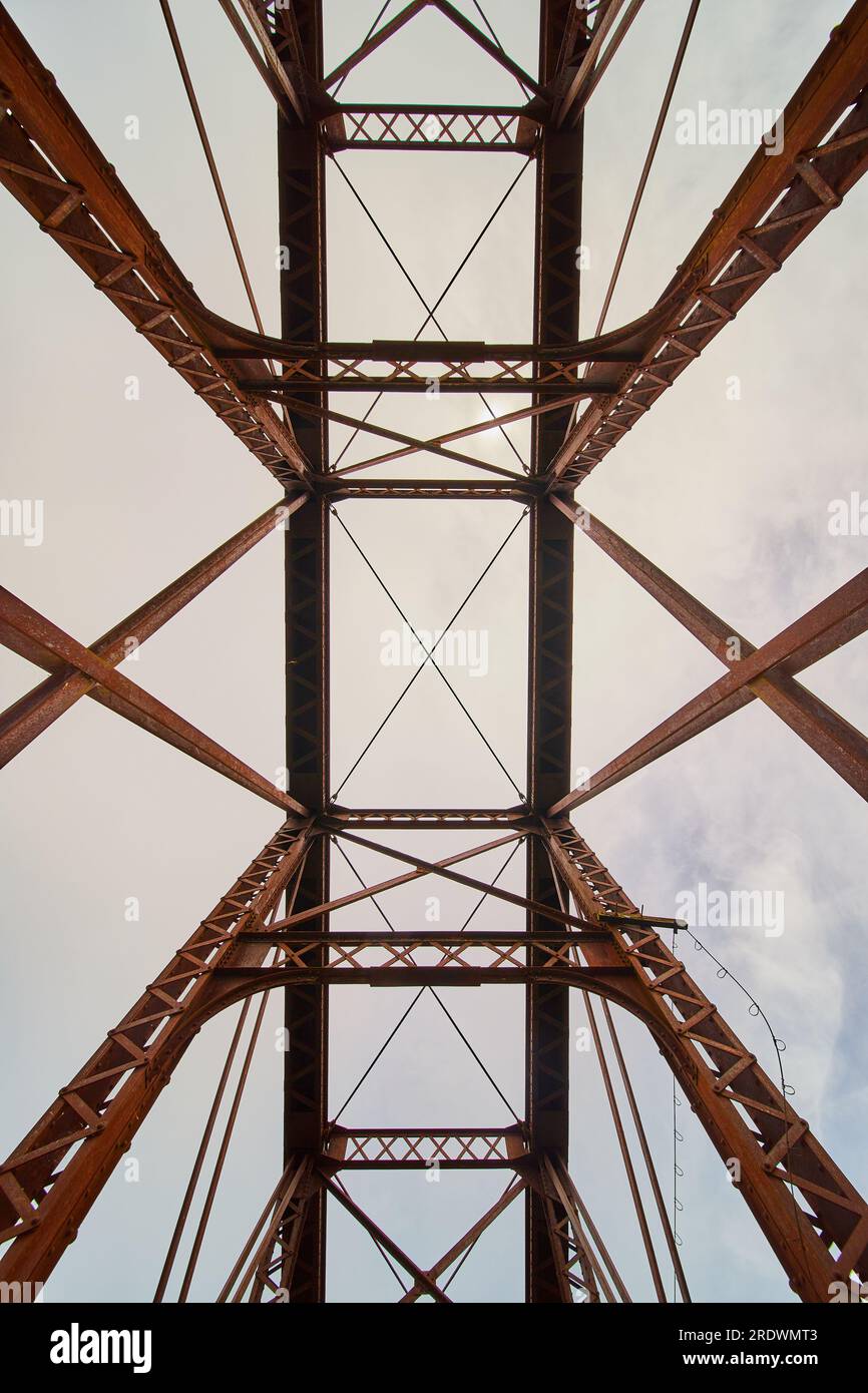 Immagine verticale del ponte ferroviario in metallo arrugginito con angolo verso l'alto del cielo attraverso fasci geometrici Foto Stock