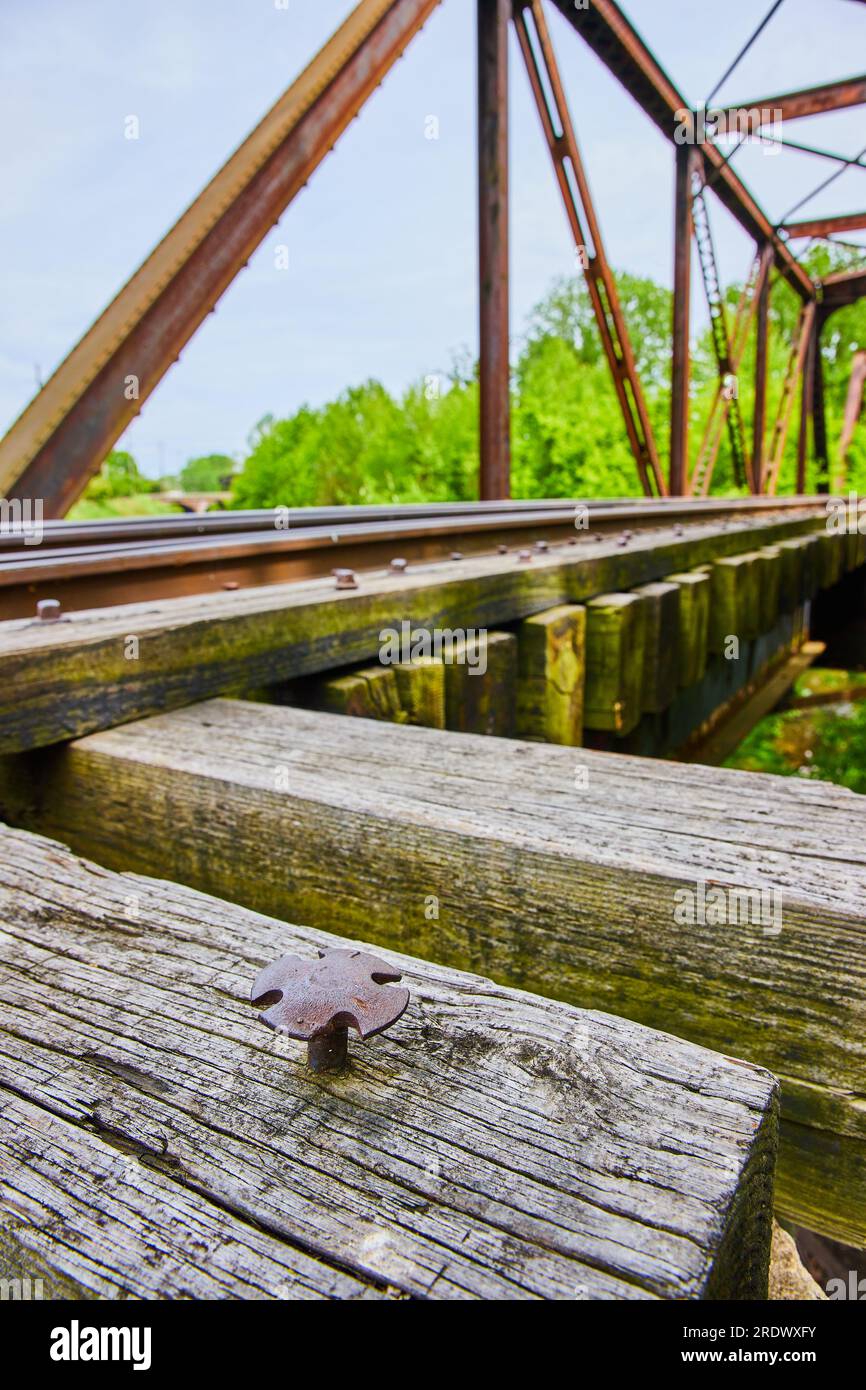 Chiodo a croce che fuoriesce dalla trave di legno su un ponte ferroviario in metallo lungo con binari Foto Stock