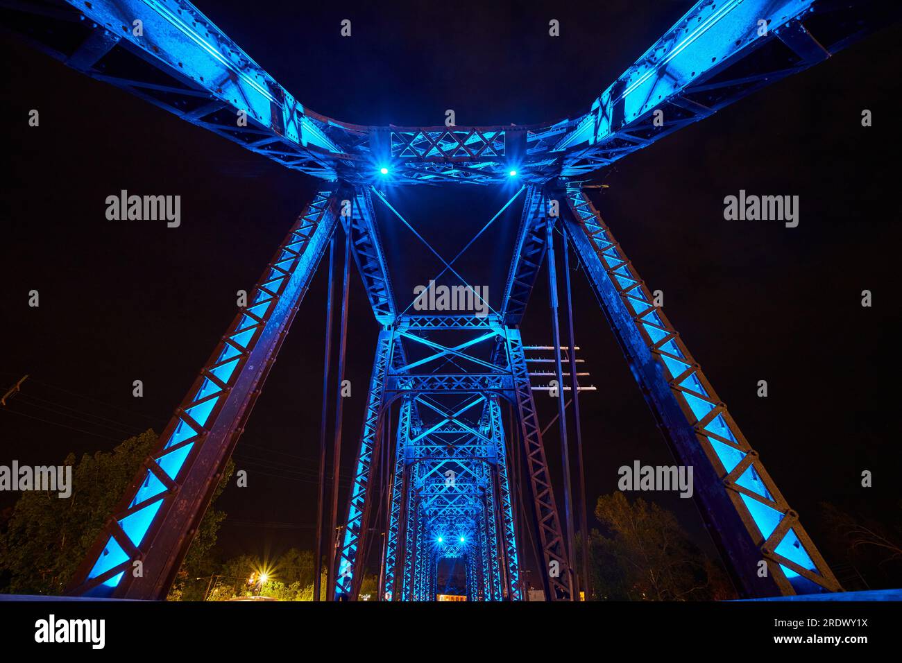 Vista verso l'alto del ponte ferroviario in ferro di notte con luci al neon blu e cielo nero Foto Stock