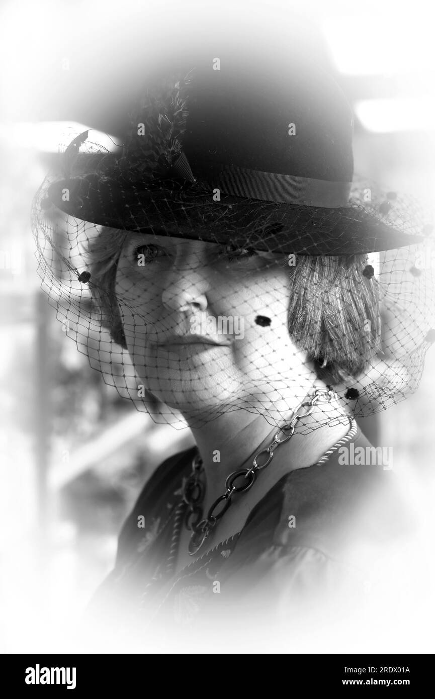 Ritratto in bianco e nero di una donna che indossa un cappello nostalgico con rete. Lei è solenne e sogna i vecchi tempi. La foto ha una morbidezza da sogno. Foto Stock