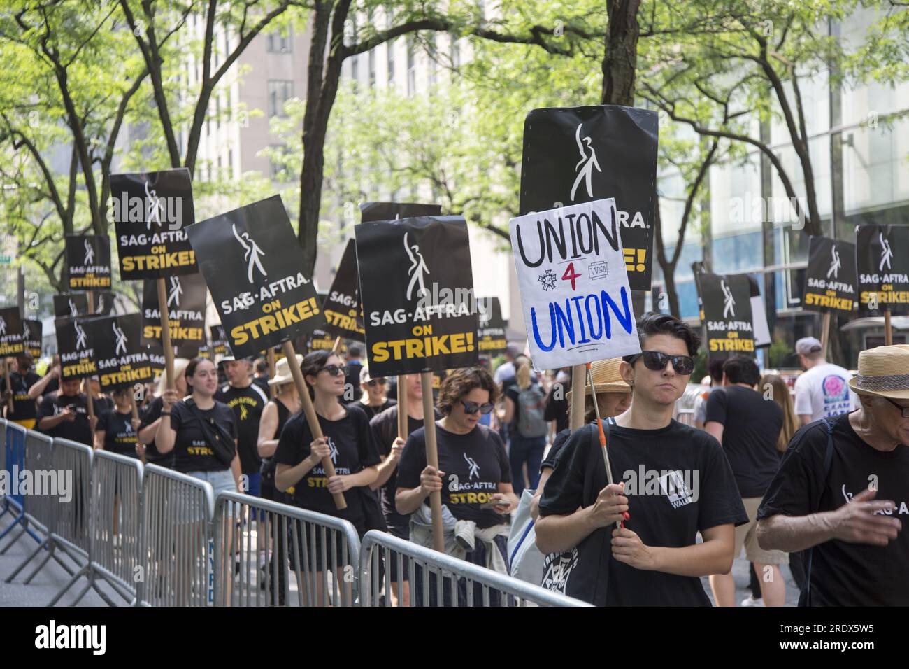 New York City: Lo sciopero continua tra gli Writers Guild of America insieme ai membri del sindacato SAG-AFTRA con linee di picchetto in più località a Manhattan. Gli scioperanti si esibiscono all'esterno degli NBC Studios sulla W. 49th Street del Rockefeller Center, paralizzando l'industria dello spettacolo. Foto Stock