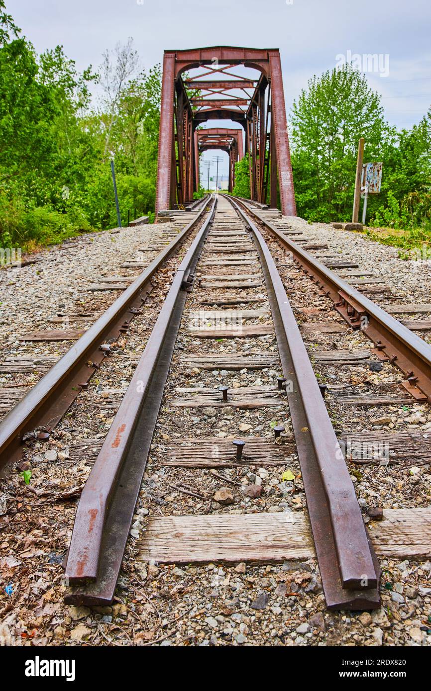 Binario ferroviario esterno attraverso un ponte arrugginito con capriate di ferro con estremità del binario centrale Foto Stock