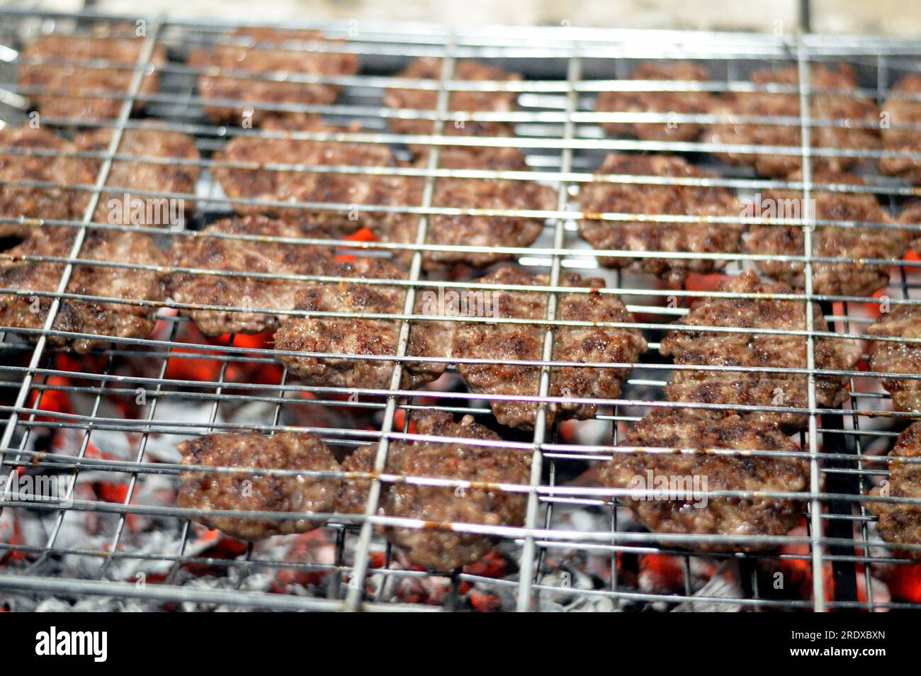 Polpette alla griglia kofta kufta di carne macinata di manzo in una rete a rete grigliata con manico su un carbone con fuoco e fuoco alla griglia, barbecue succoso Foto Stock