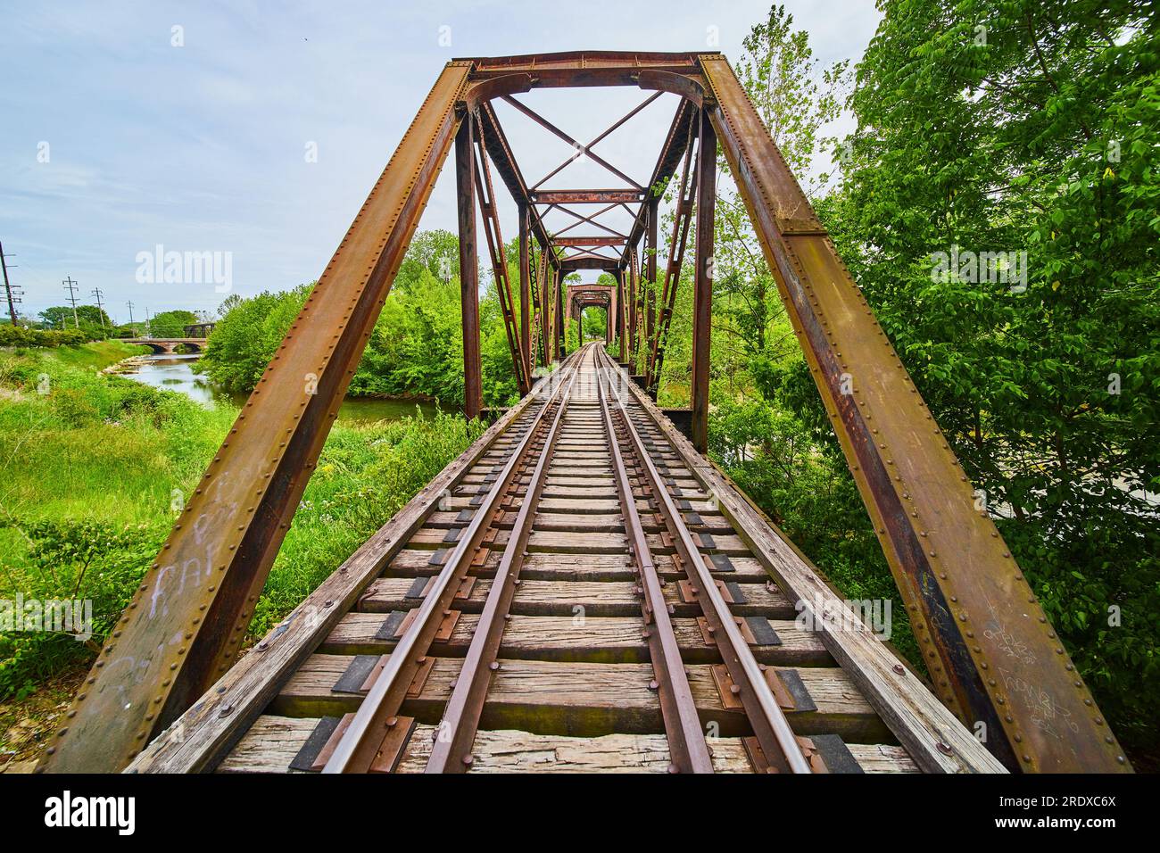 Ponte ferroviario orizzontale in ferro arrugginito con binari ferroviari che conducono all'area boschiva sopra il fiume Foto Stock