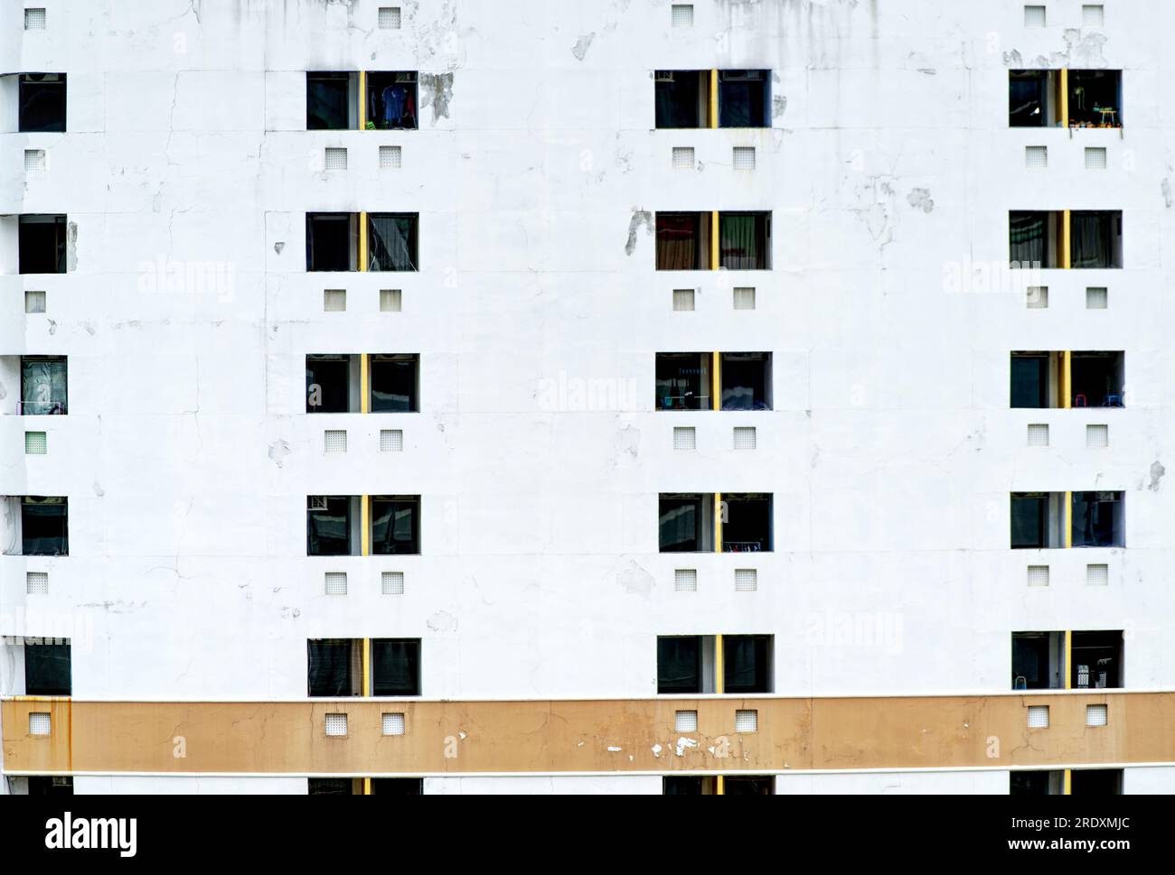 Muro all'esterno di un vecchio condominio o appartamento con pareti incrinate, struttura vecchia, condizioni atmosferiche, vecchi dipinti e motivi di finestre. Foto Stock