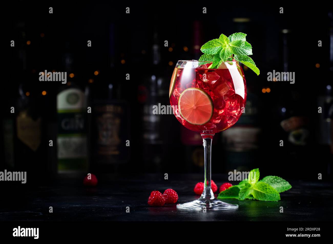 Cocktail alcolico Royal limonade con tequila, gin secco, rum bianco, vodka, liquore, lime, lamponi e ghiaccio nel bicchiere da vino. Bancone bar nero ba Foto Stock