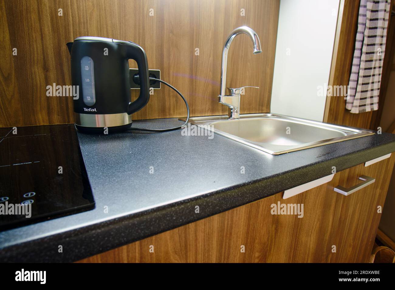 La piccola cucina dell'appartamento compatto presenta una stufa nera e un bollitore Tefal - Tula, Russia, 4 luglio 2023 Foto Stock