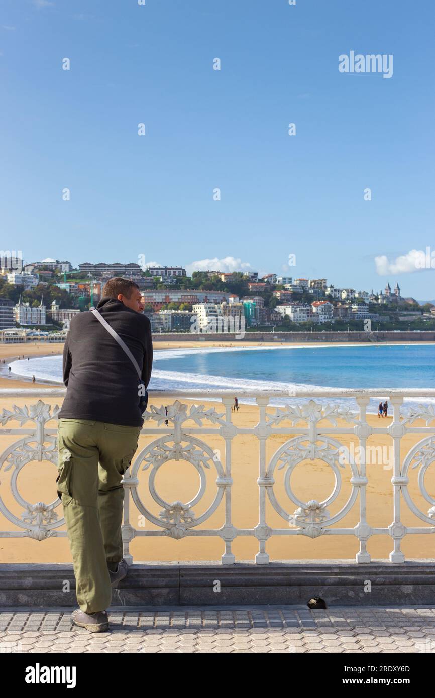 Uomo da dietro sulla spiaggia la Concha di Biscay Bay. San Sebastian Landmark, Paesi Baschi, Spagna. Costa panoramica con turisti solitari. Perditi Foto Stock