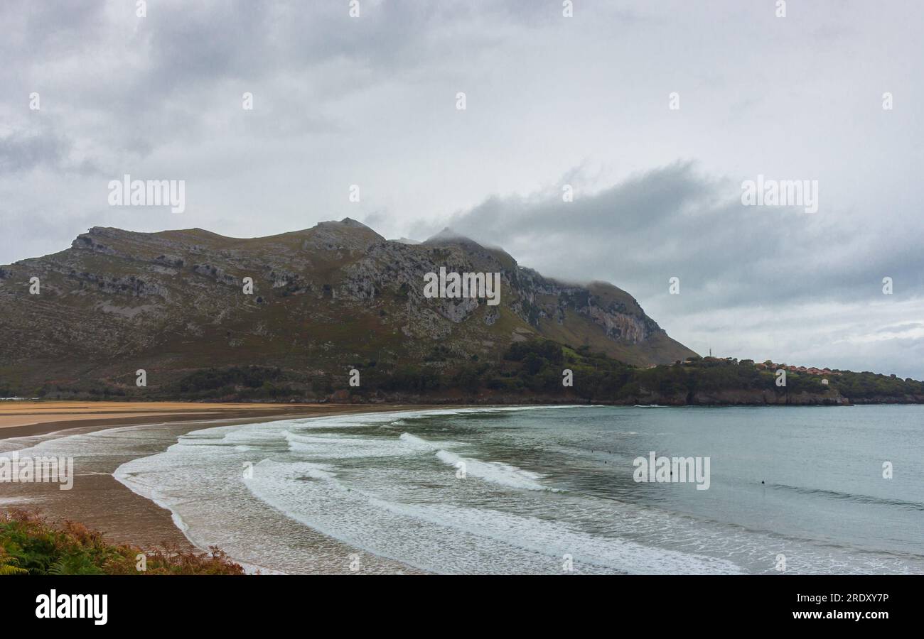 Ampia spiaggia per il surf con la montagna tra nuvole. Paesaggio autunnale con costa vuota. Paesaggio marino turchese. Paesaggio di Camino de Santiago. Turismo in Spagna. Foto Stock