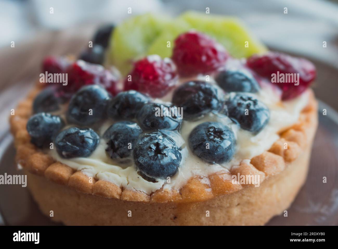 Torta gustosa con frutti di bosco freschi da vicino. Crostata fatta in casa con mirtilli, lamponi e fette di kiwi. Delizioso dessert. Colazione dolce. Foto Stock