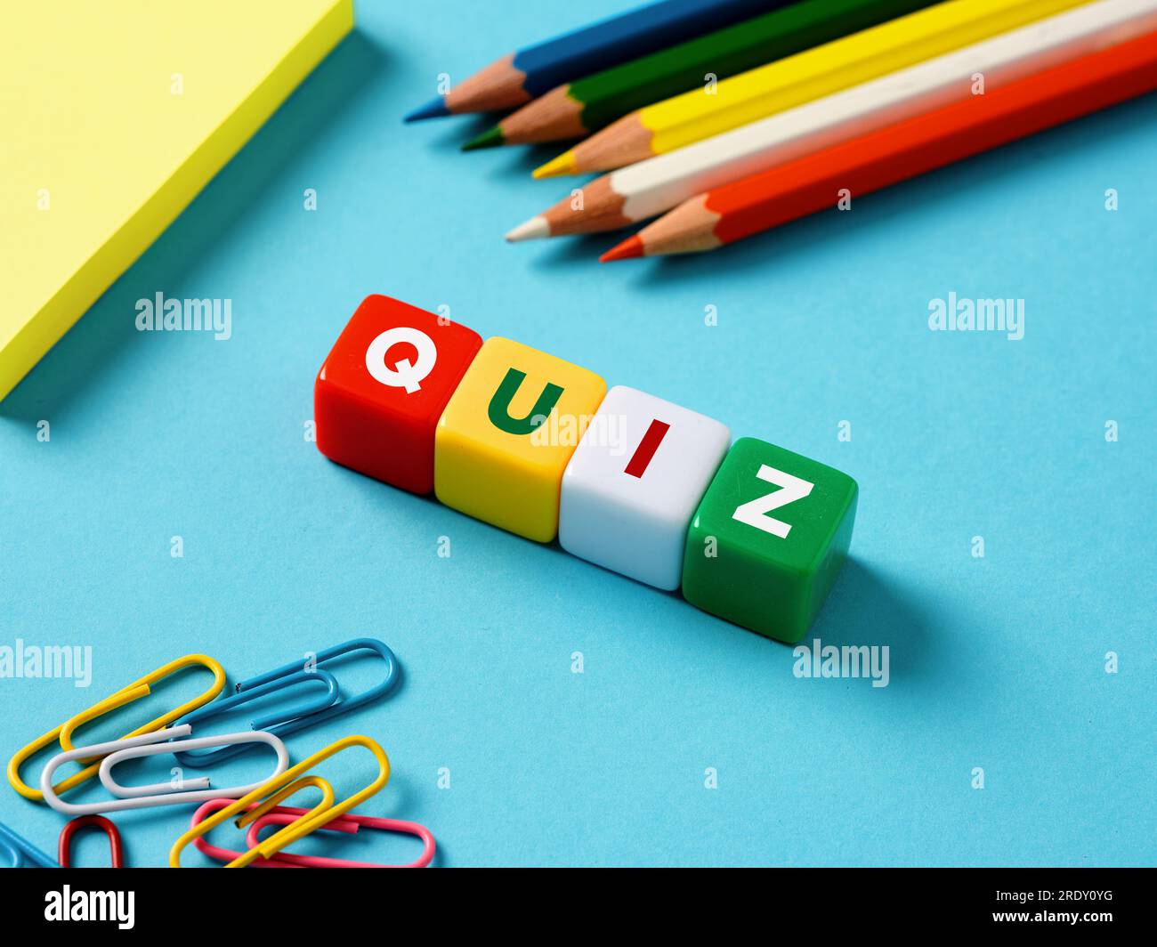 Concetto di esame didattico o gioco di domande. Il quiz di parole su cubi colorati con oggetti di cancelleria su sfondo blu. Foto Stock