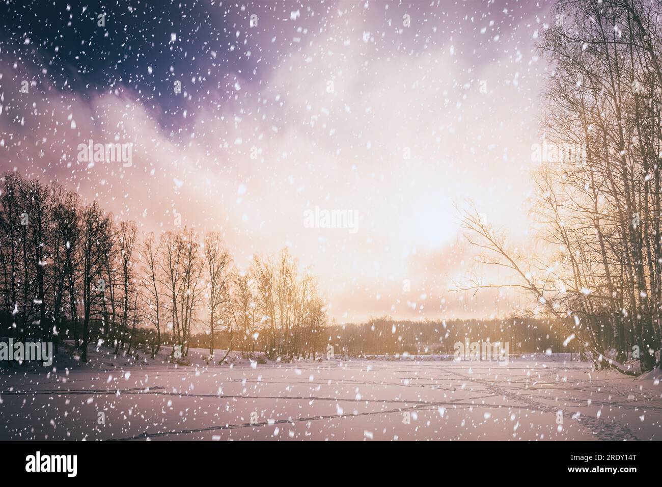 Tramonto o alba su uno stagno ghiacciato con betulle lungo le rive e neve che cade in inverno. Nevicate. L'estetica della pellicola vintage. Foto Stock