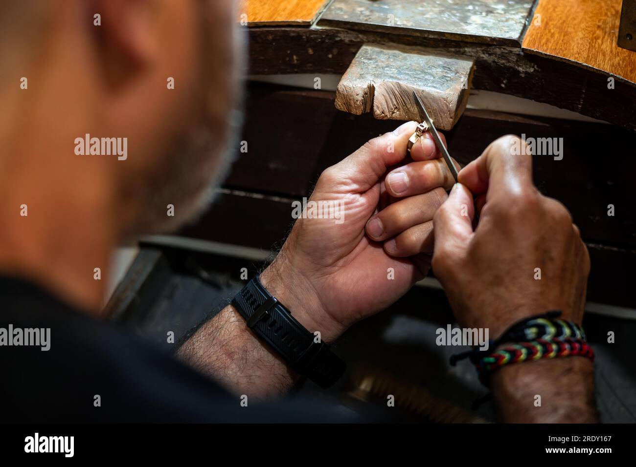 Orafo gioielliere che lavora nel suo laboratorio di gioielleria artigianale creando e limando un gioiello in oro bianco o argento nel suo studio di lavoro. Foto Stock