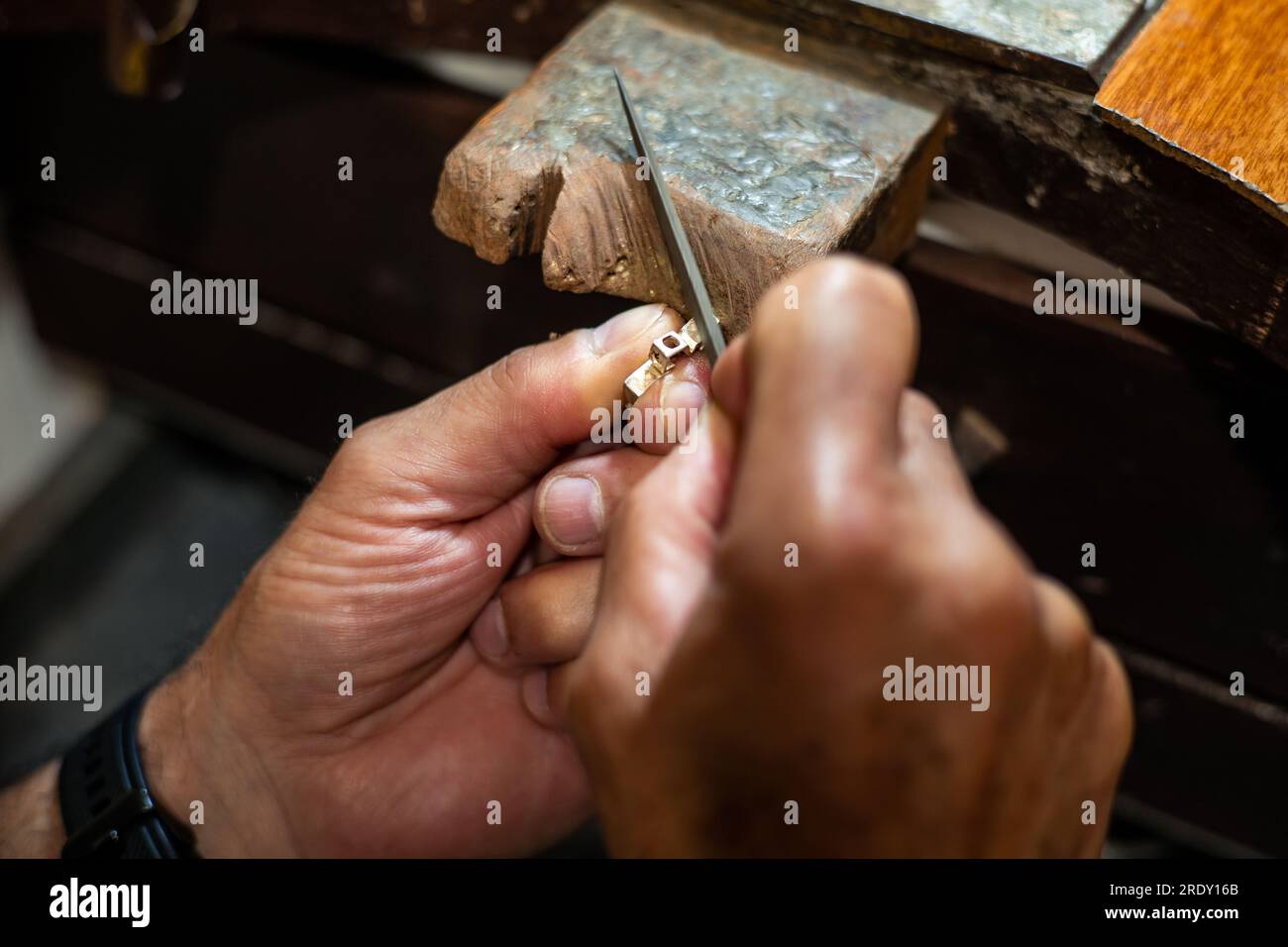 Orafo gioielliere che lavora nel suo laboratorio di gioielleria artigianale creando e limando un gioiello in oro bianco o argento nel suo studio di lavoro. Foto Stock