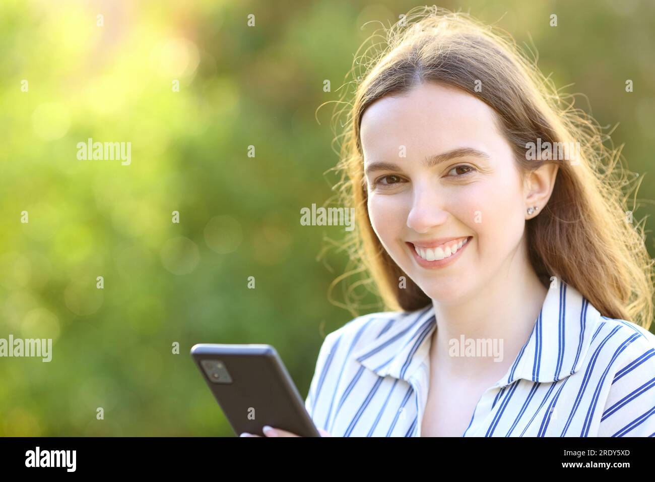 Happy Woman tiene lo smartphone e ti guarda in un parco Foto Stock