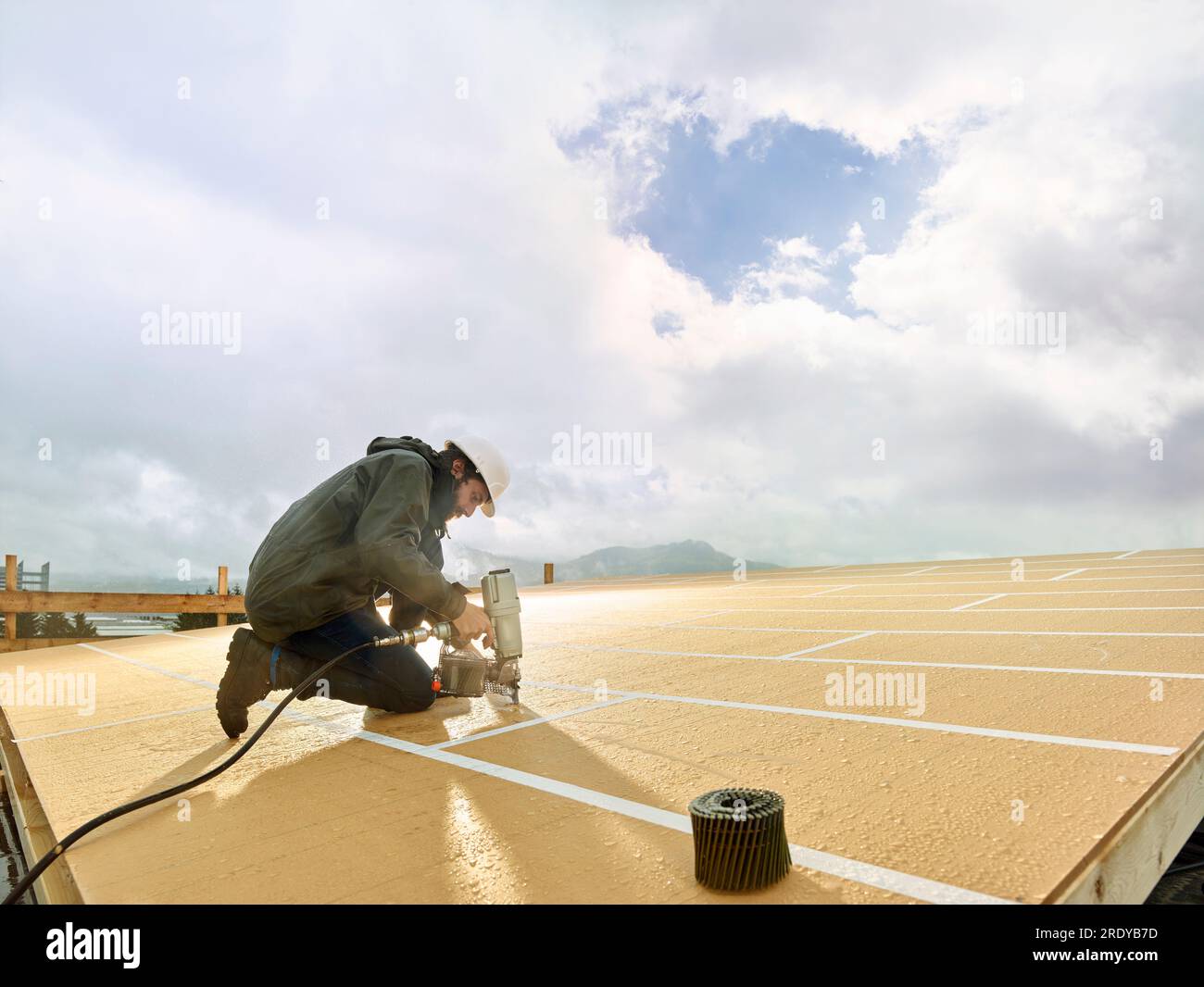 Carpentiere che utilizza un utensile per chiodi sul tetto in legno in cantiere Foto Stock