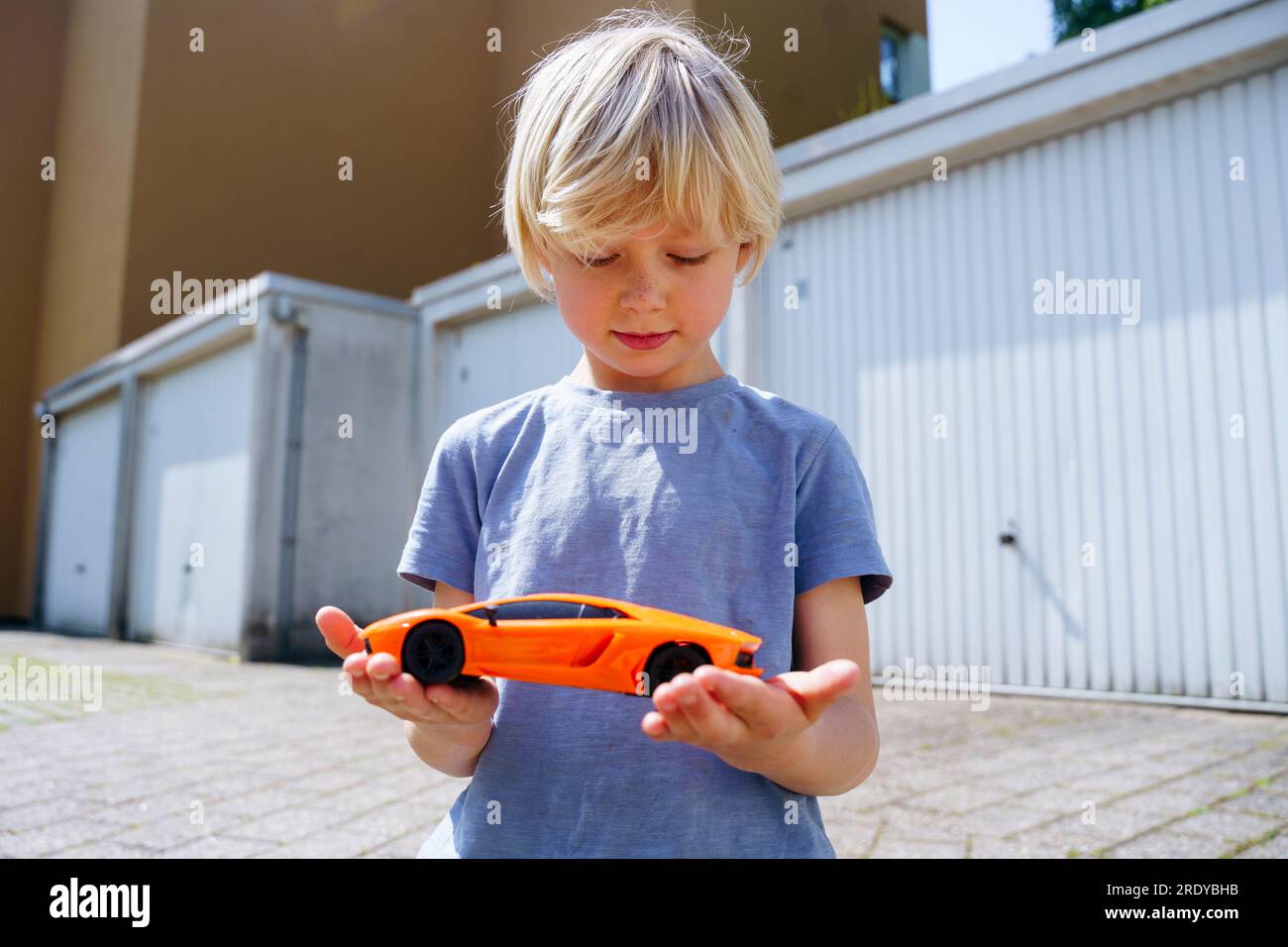 Ragazzo che tiene un'auto giocattolo nel cortile fuori dal garage Foto Stock