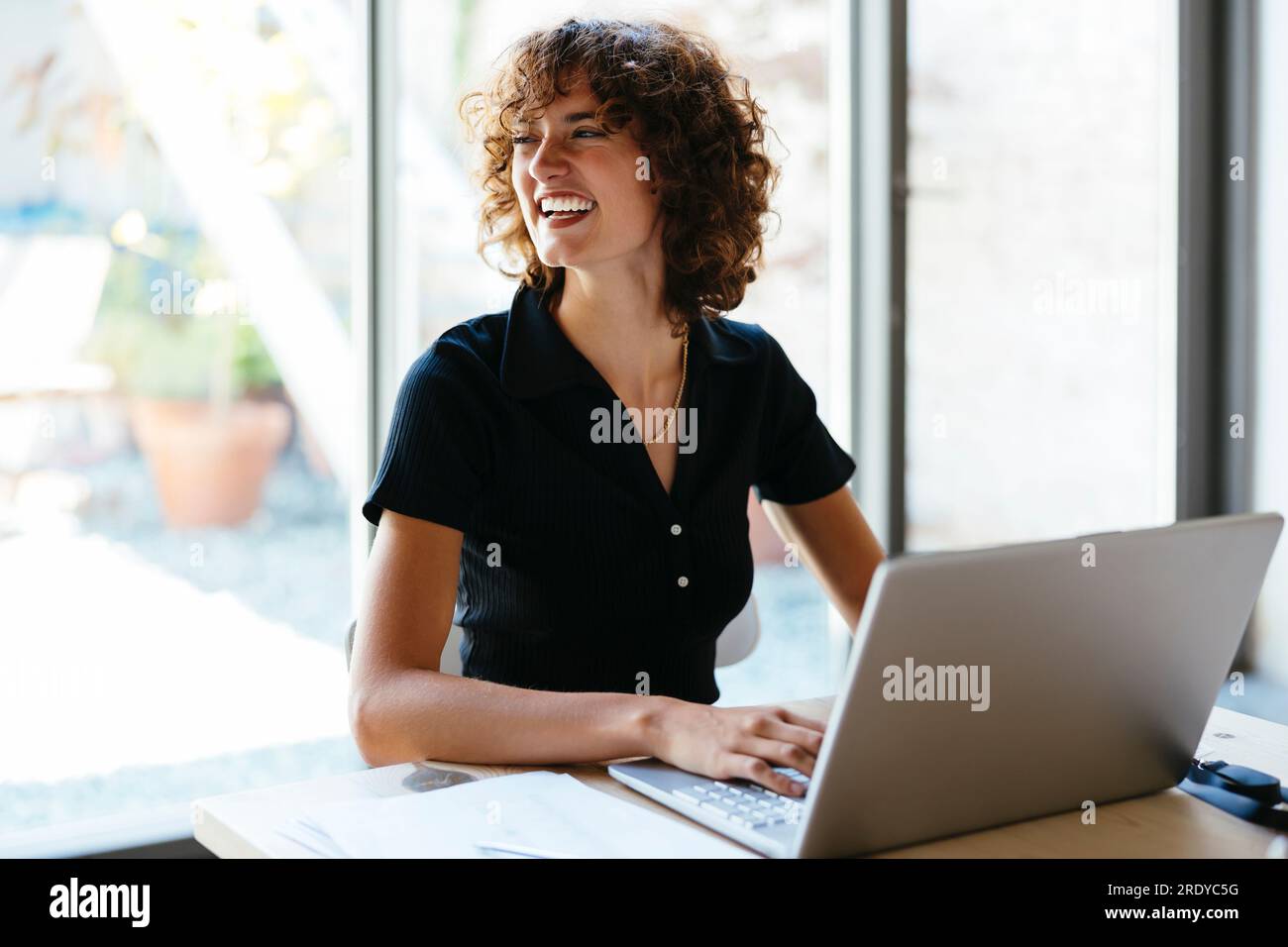 Felice giovane donna d'affari seduta con un computer portatile alla scrivania Foto Stock