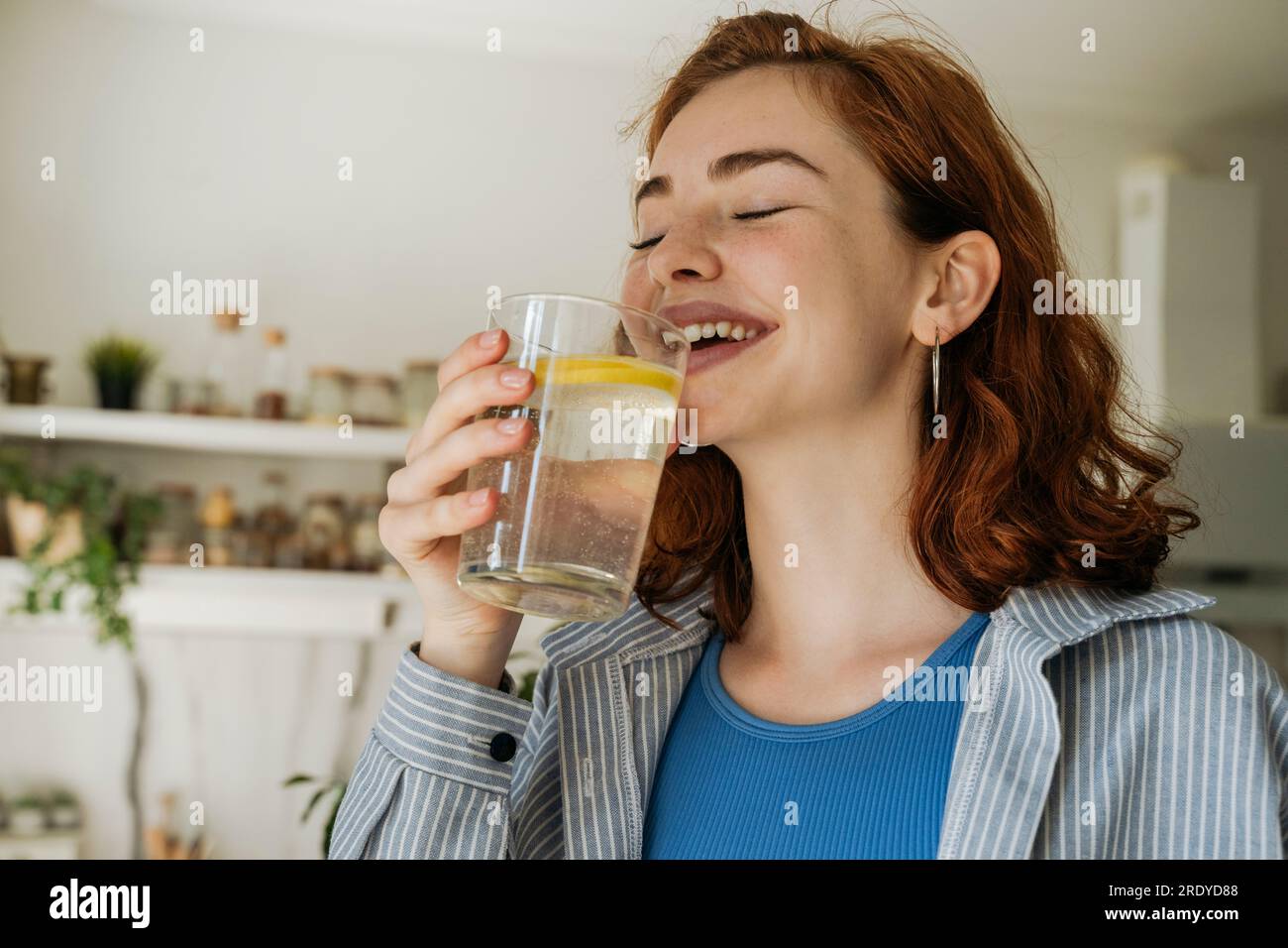 Felice donna rossa che beve acqua a casa Foto Stock