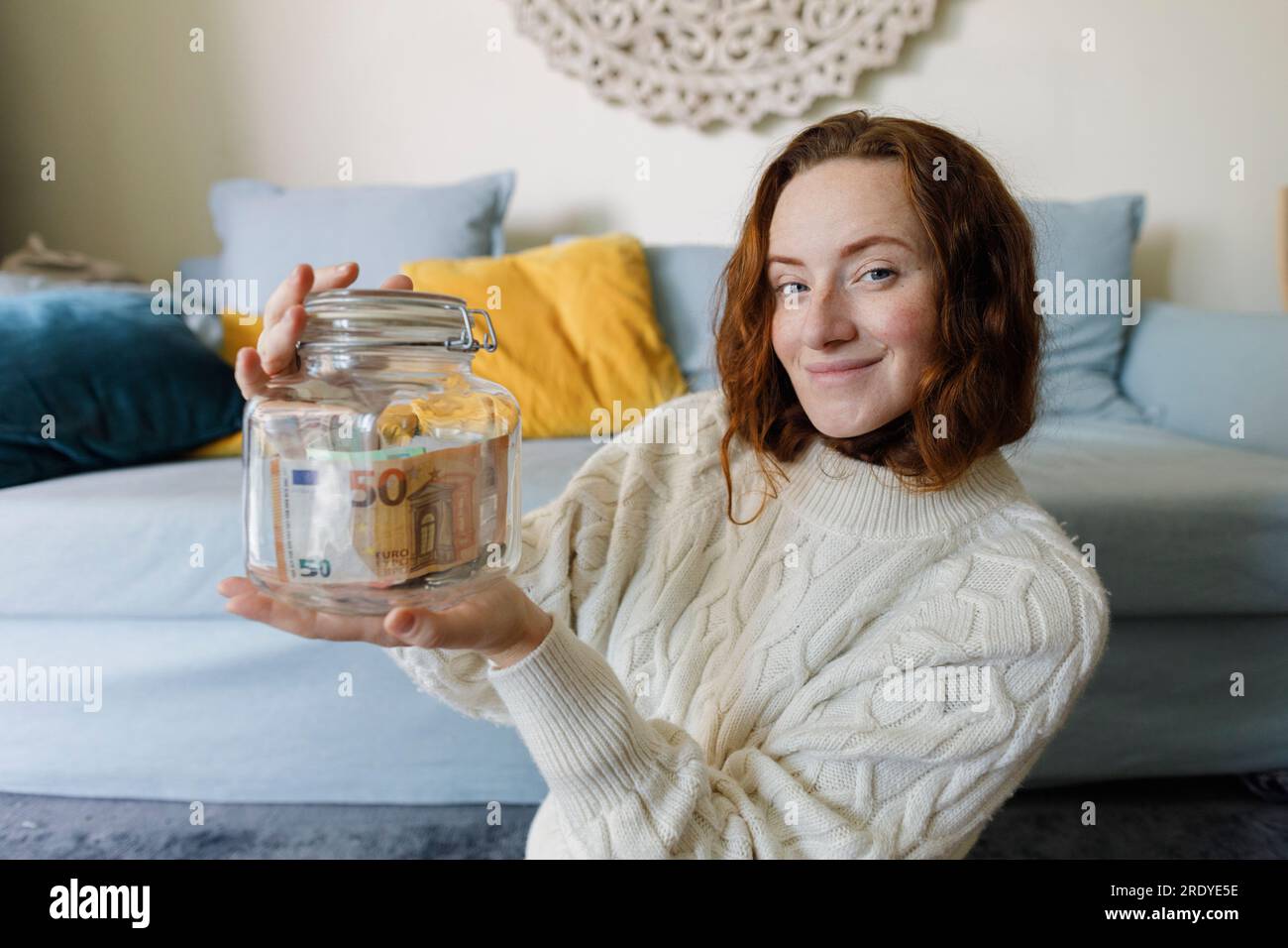 Donna sorridente che tiene un barattolo di risparmio a casa Foto Stock