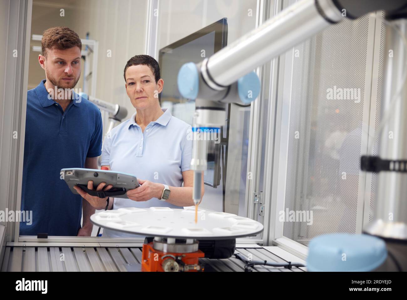 Colleghi che esaminano il braccio robotico utilizzando apparecchiature industriali Foto Stock