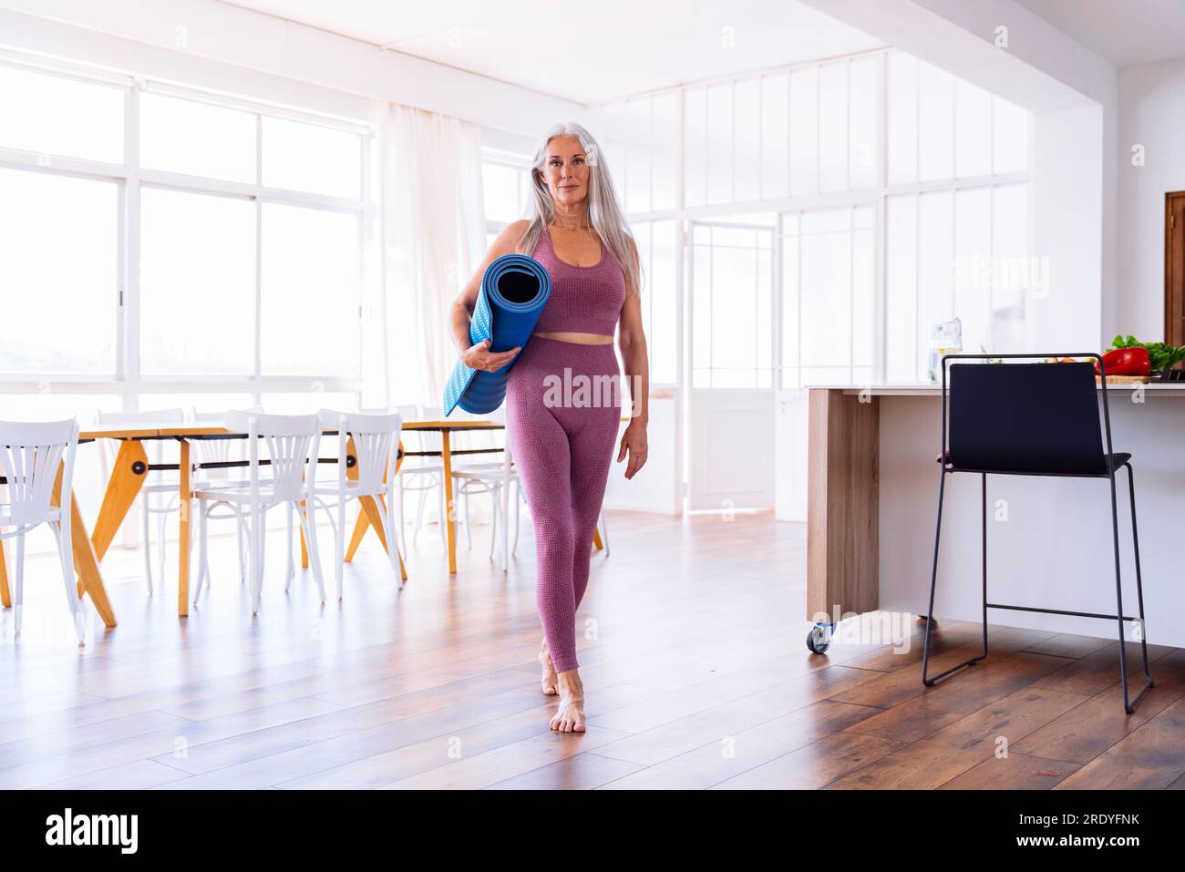 Donna che tiene un tappetino yoga che cammina a casa Foto Stock