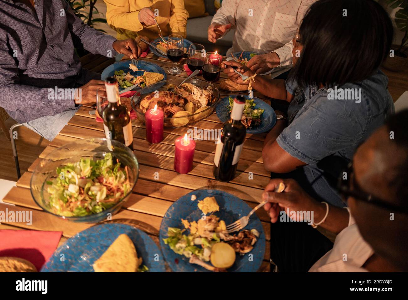 Amici anziani multiculturali che mangiano cibo e vino con candele sul tavolo da pranzo Foto Stock