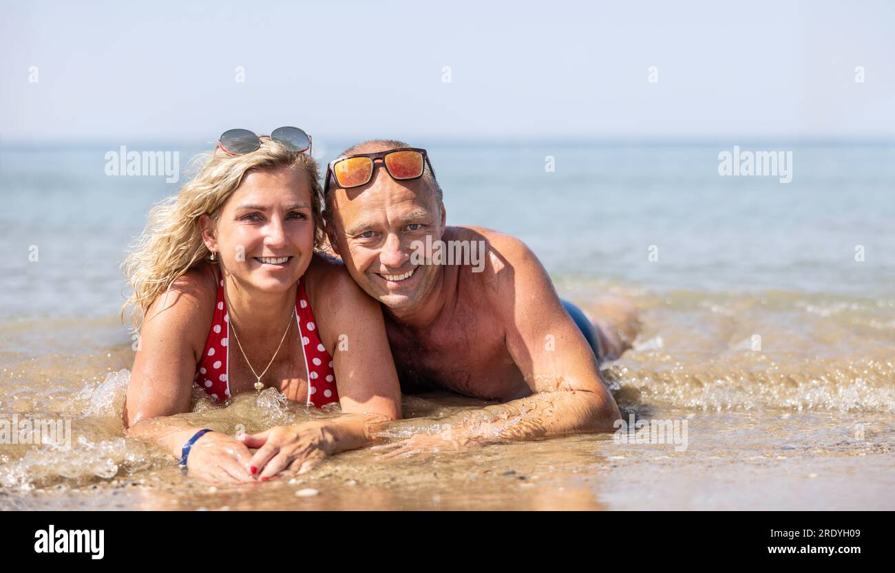 Una coppia di mezza età sdraiata su una spiaggia vicino al mare durante una calda giornata estiva; trascorre una vacanza insieme. Foto Stock