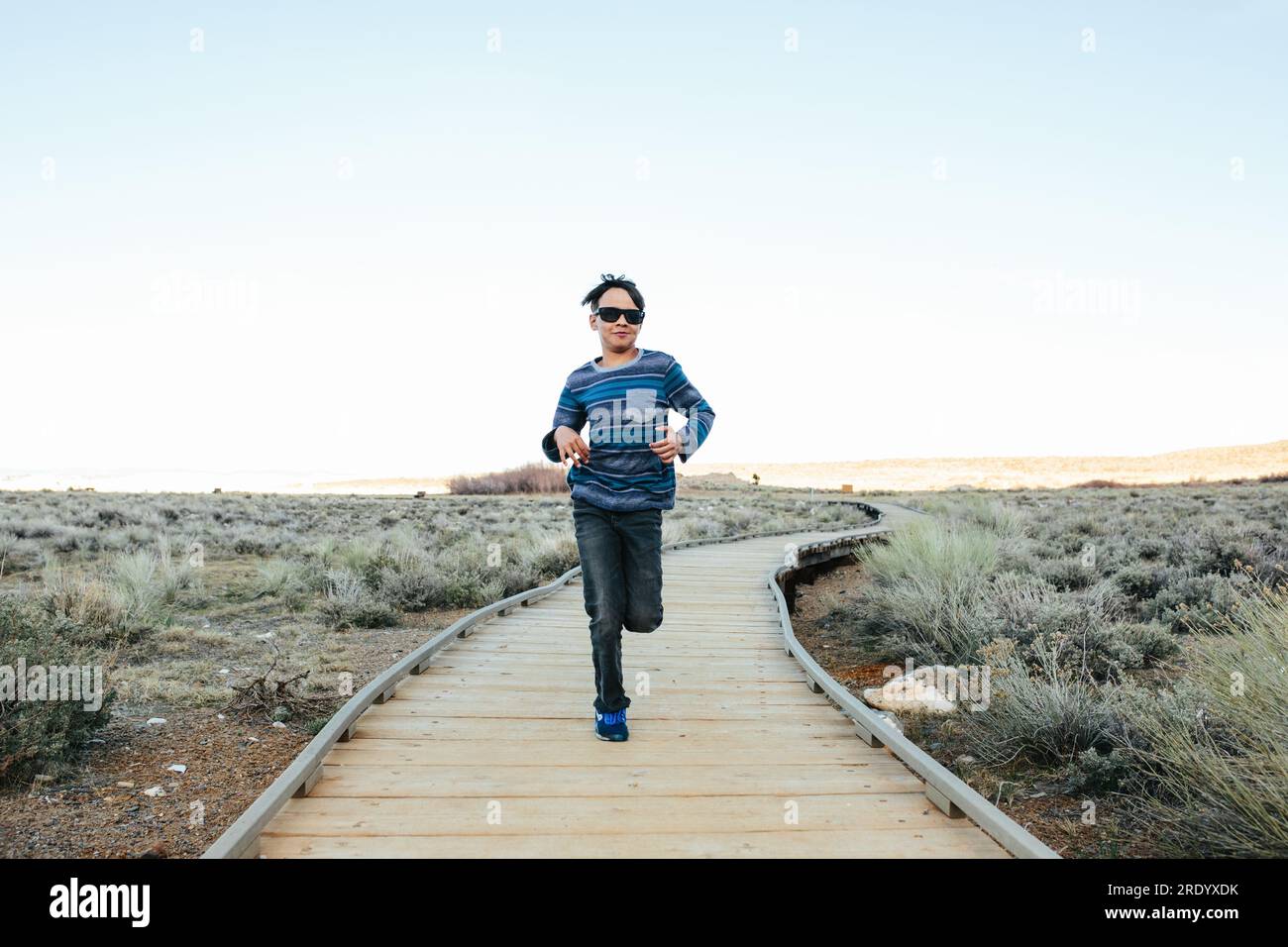 Il ragazzo che indossa gli occhiali da sole corre verso la macchina fotografica su una passerella Foto Stock