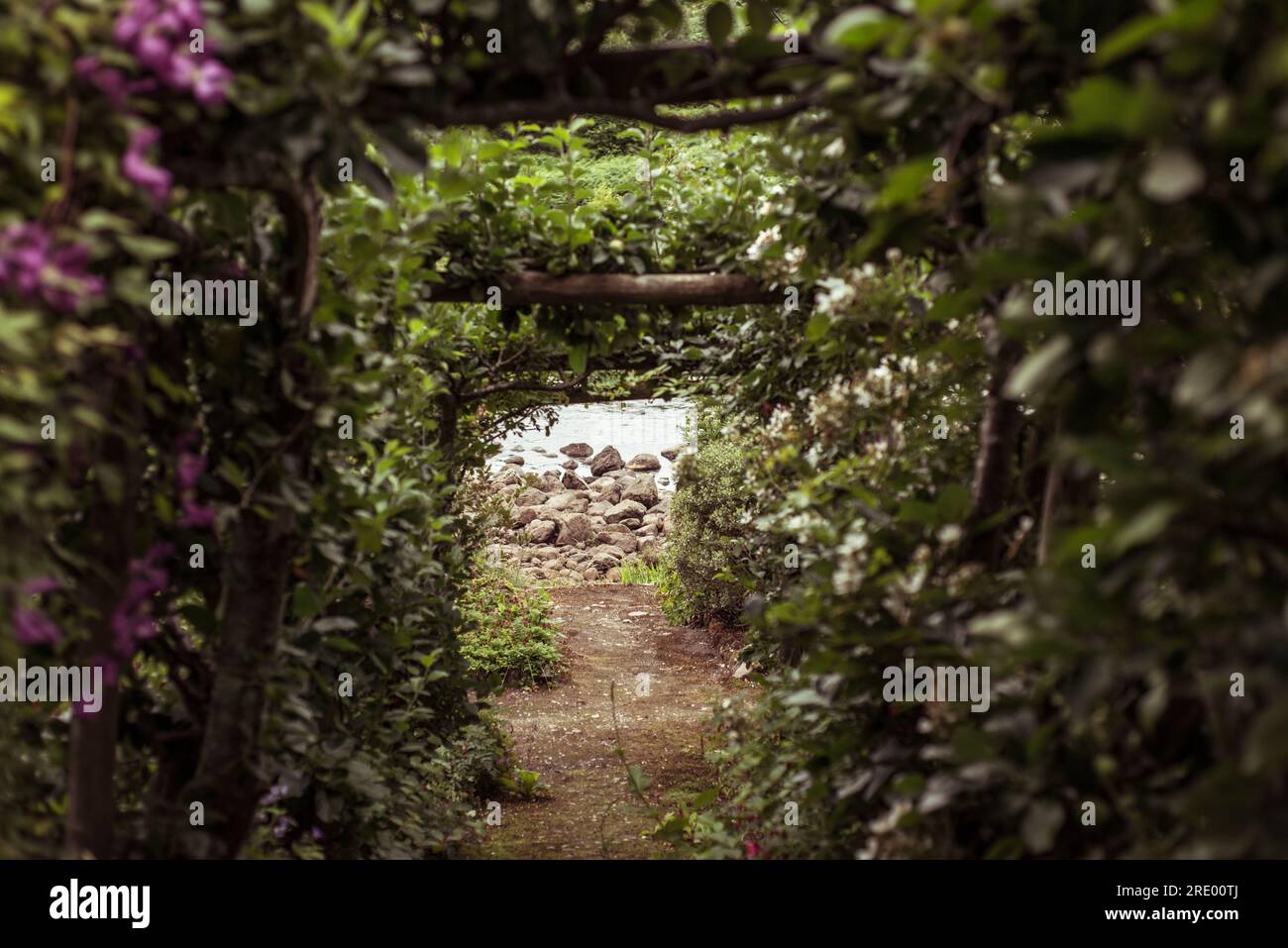Grazioso sentiero giardino con arco fiorito che conduce al fiume Foto Stock