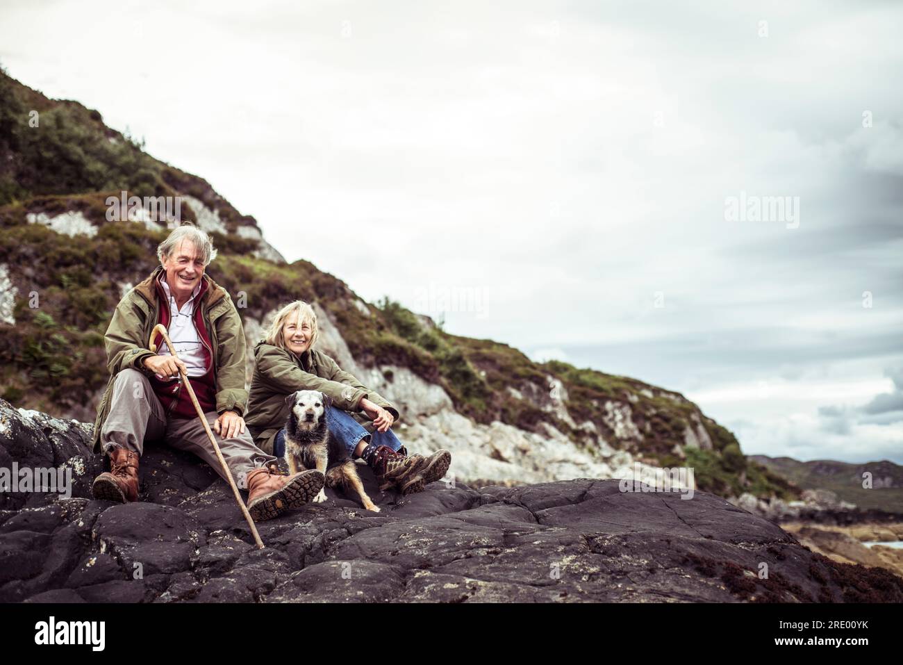 la coppia in pensione siede con un cane sulle rocce vicino all'oceano nell'aspra scozia Foto Stock