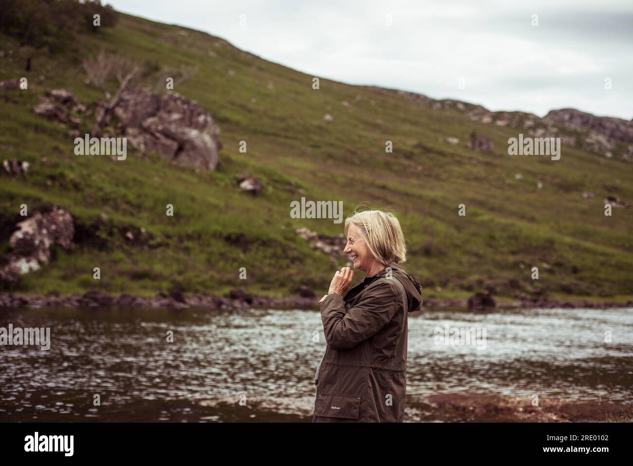 la donna in pensione ride e sorride lungo un remoto fiume di pesca nelle highlands Foto Stock