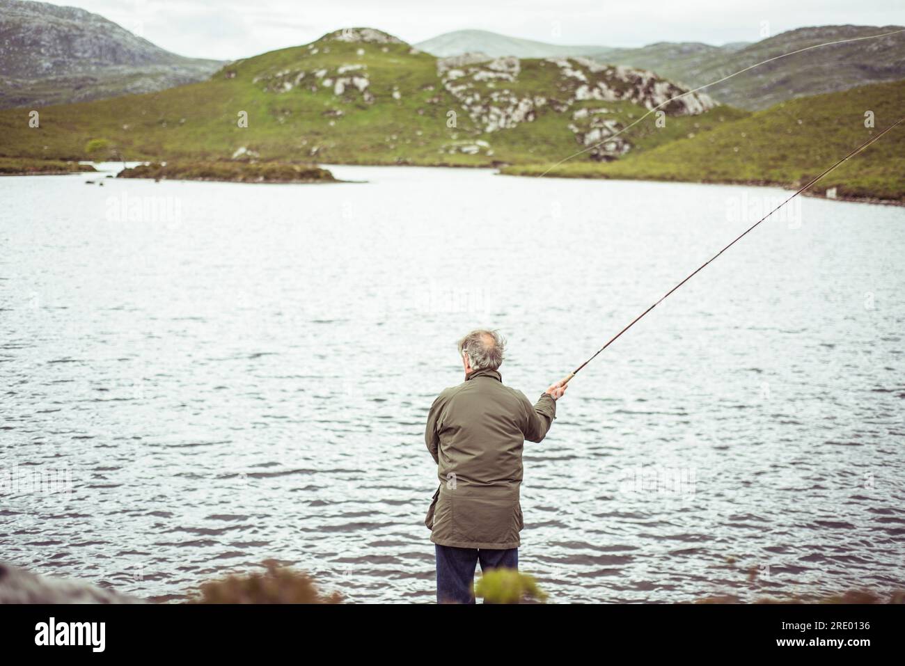 l'uomo pesca con la mosca sul lago nelle remote montagne della scozia Foto Stock
