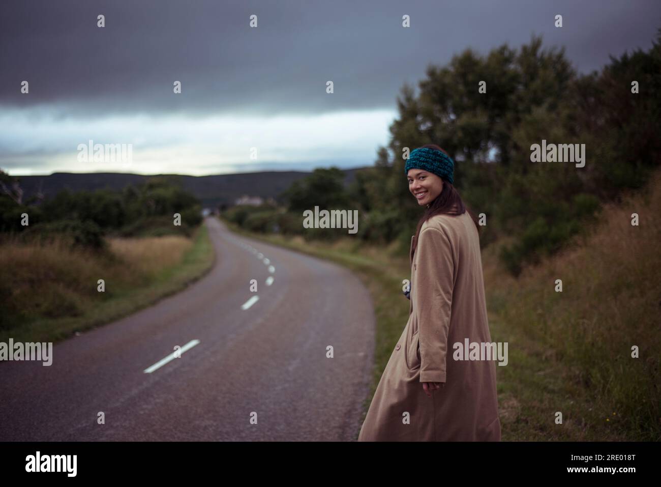 La ragazza asiatica guarda indietro e sorride camminando lungo una strada remota Foto Stock