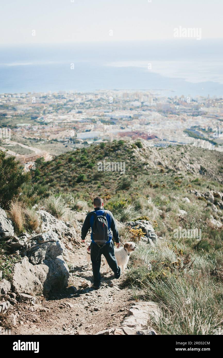 Uomo che cammina lungo una collina con un cane che si affaccia sulla città e sull'oceano di Malaga Foto Stock